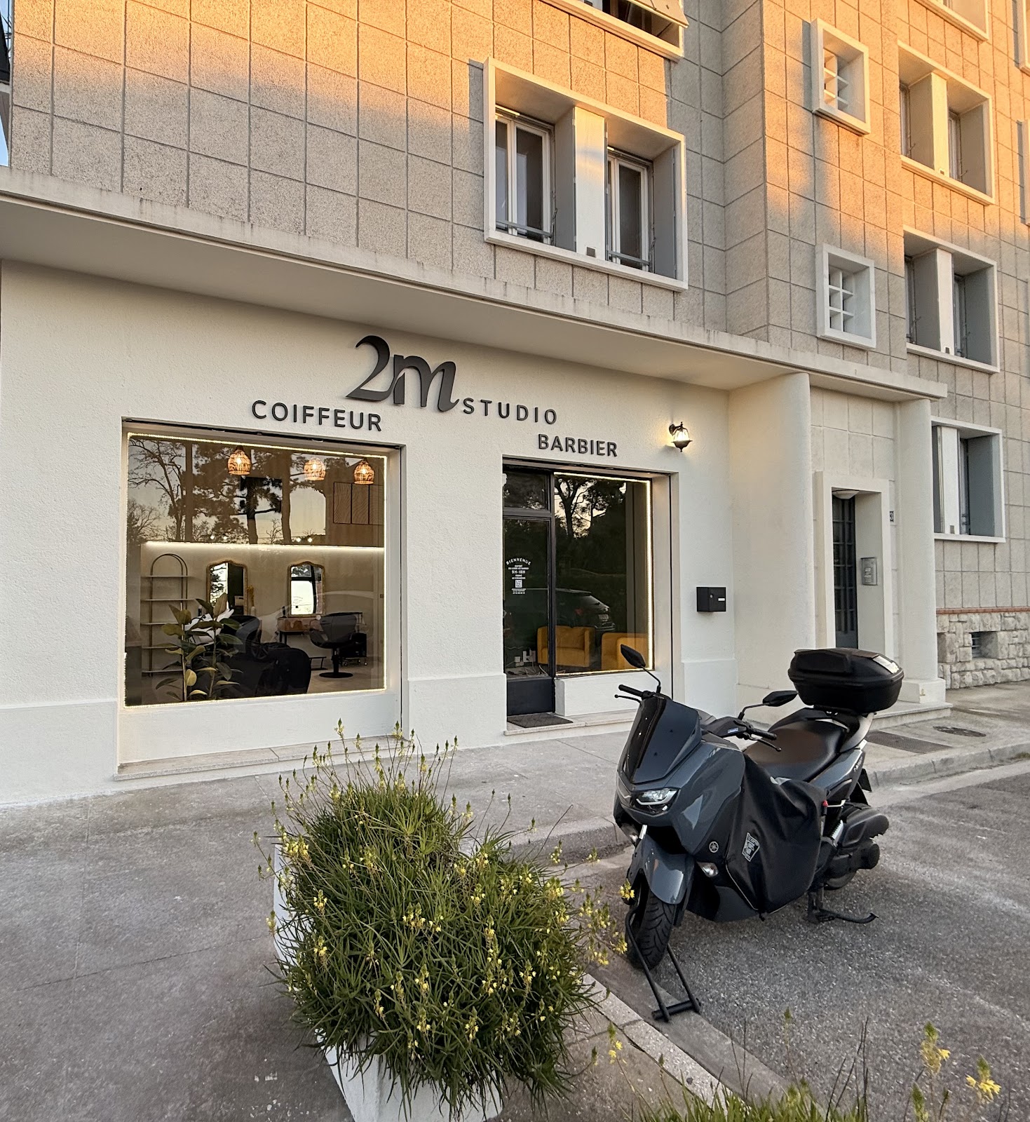 Storefront at dusk with scooter parked outside, 2M Coiffeur Barbier signage lit up