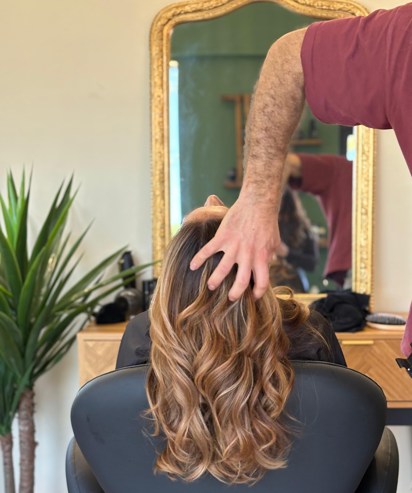 Brunette wavy hair styled, seen from behind near a gold-framed mirror